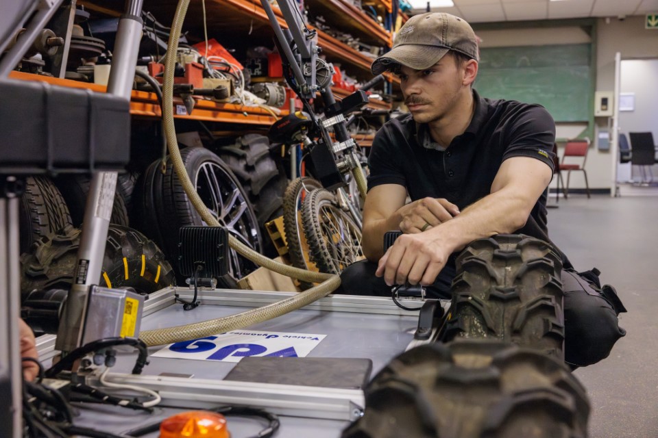 Man with cap kneels next to an open vehicle chassis in a workshop setting