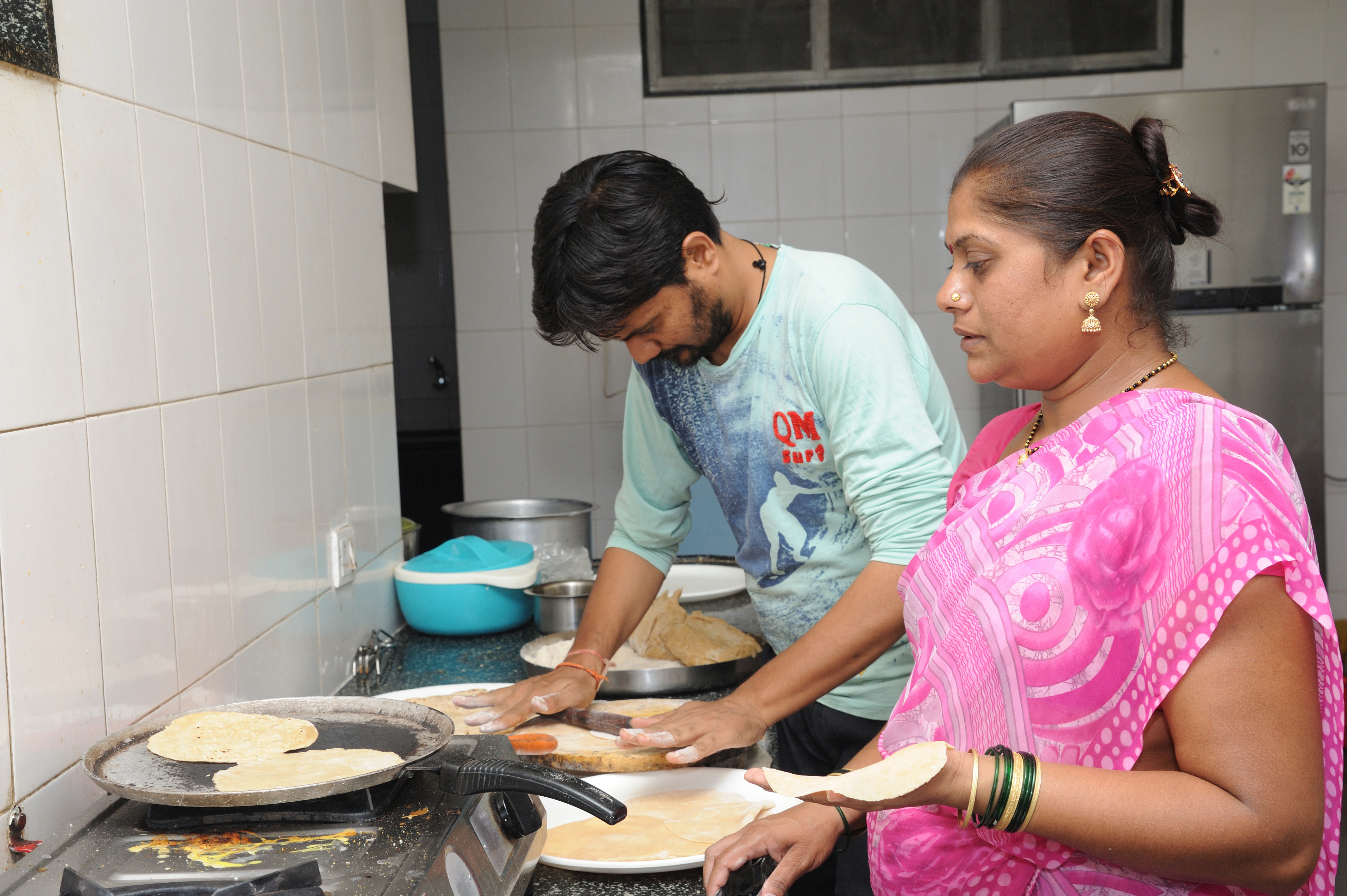 A man and woman cook over a stove.