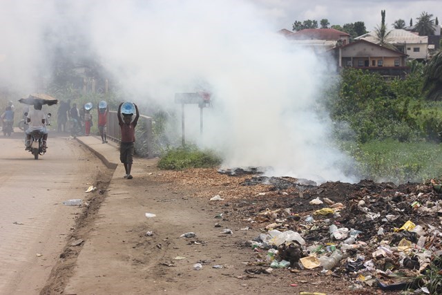 Children carry water next to smouldering waste in Douala, Cameroon; ©WasteAid
